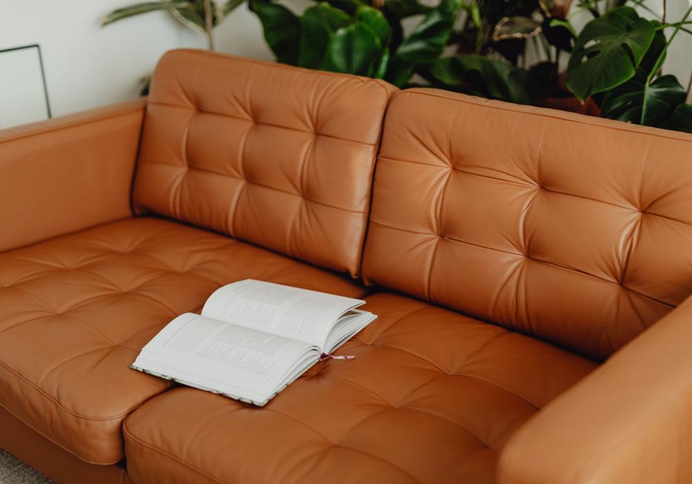 Elegant brown leather sofa with an open book, surrounded by vibrant houseplants, perfect for relaxation.